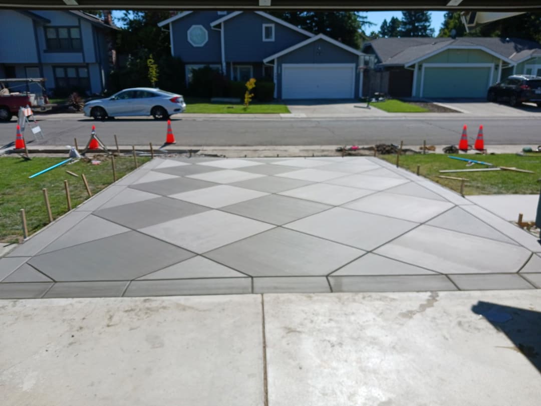 Newly finished decorative concrete driveway with geometric pattern and construction equipment nearby.