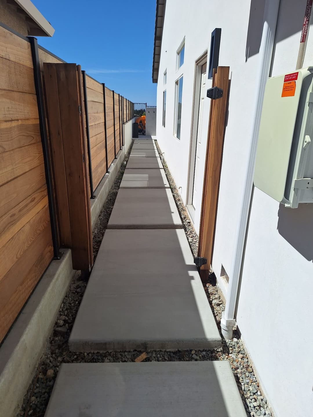 Concrete pathway alongside wooden fencing leading to the side of a modern house.