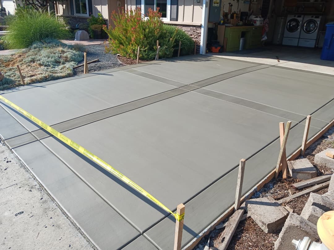 Freshly poured concrete slab with wooden forms and yellow measuring tape in residential setting.