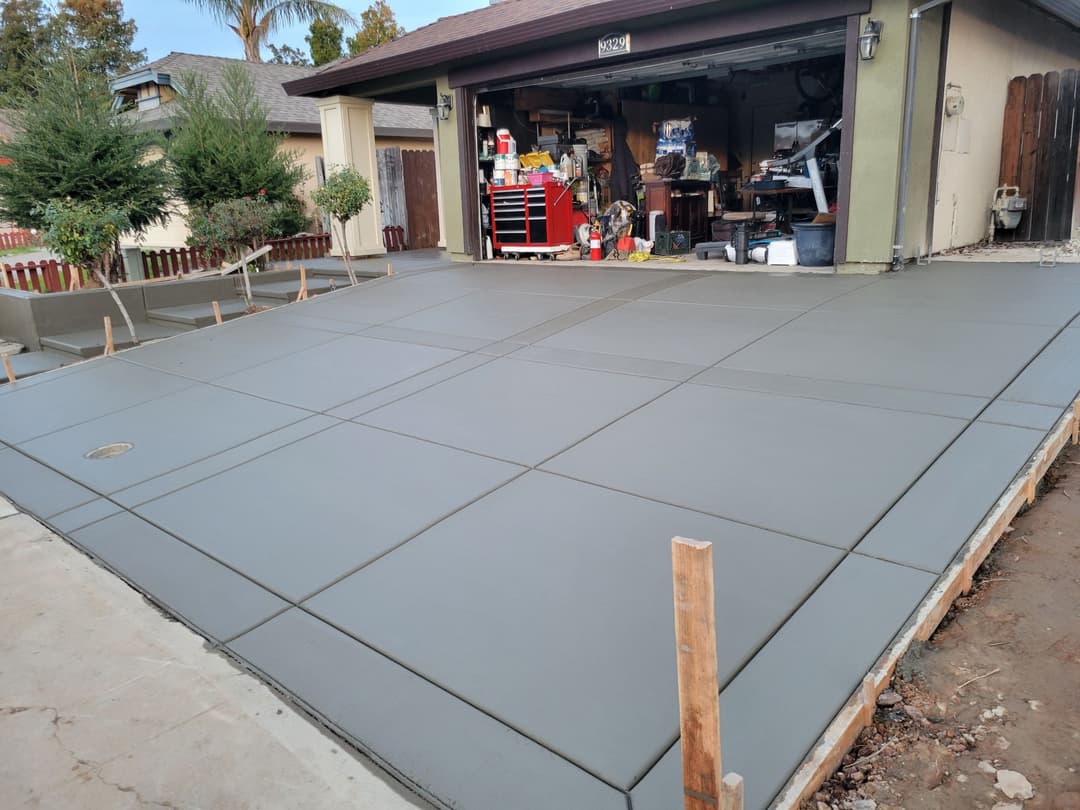 Newly poured concrete garage floor with neatly defined expansion joints and tools in background.