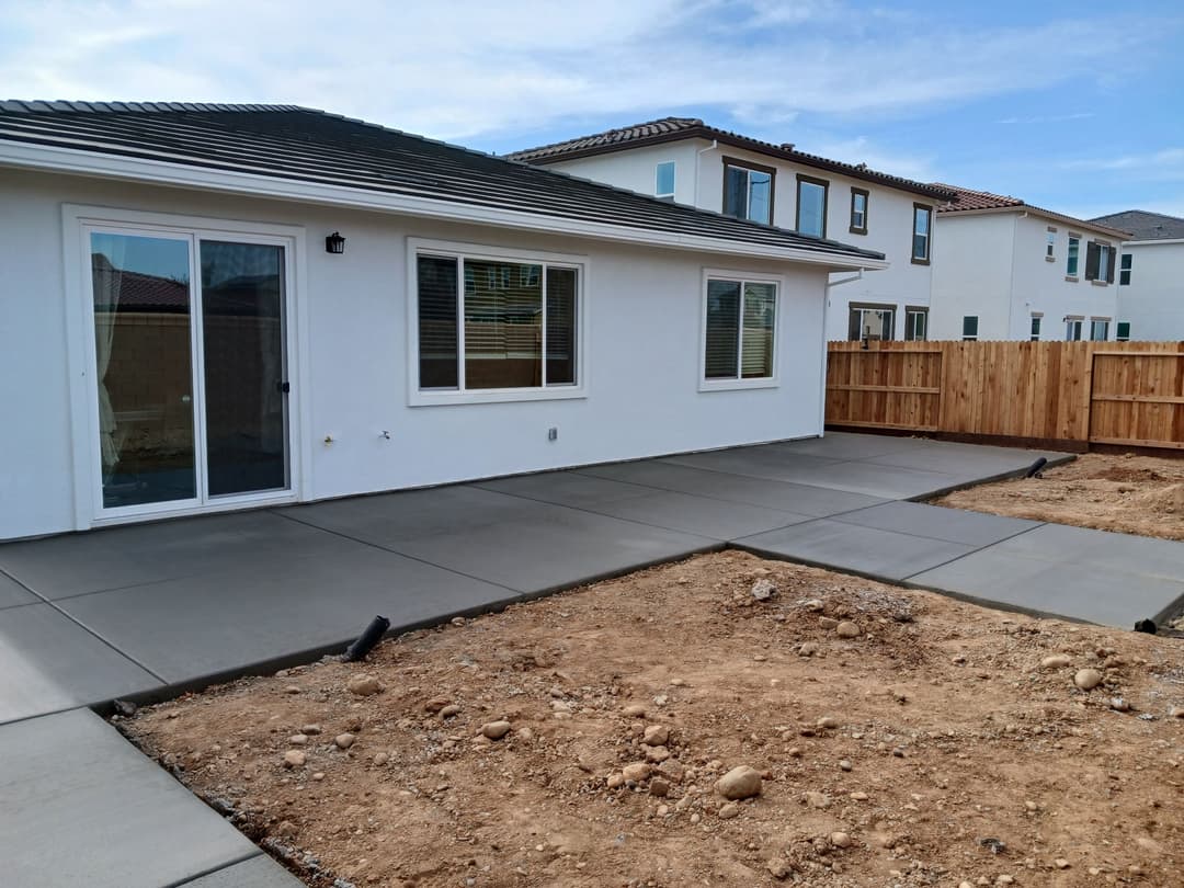 Newly poured concrete patio in a residential backyard with a fenced area and neighboring homes.