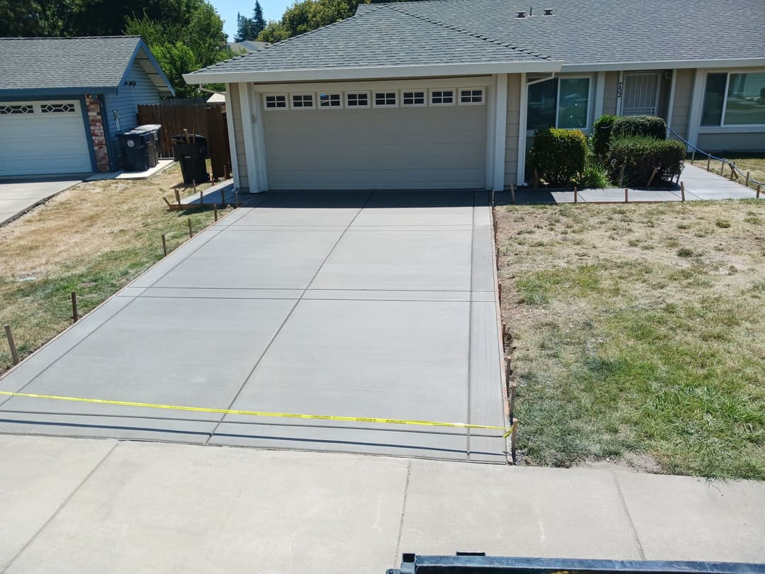Freshly poured concrete driveway with yellow caution tape in a residential neighborhood.