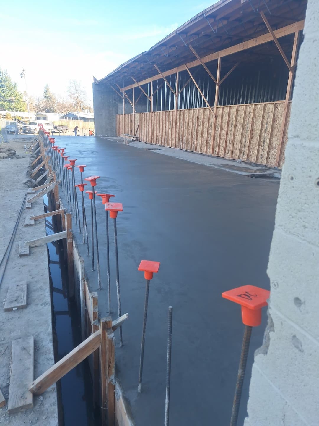 Freshly poured concrete slab with rebar and orange markers near a construction site.