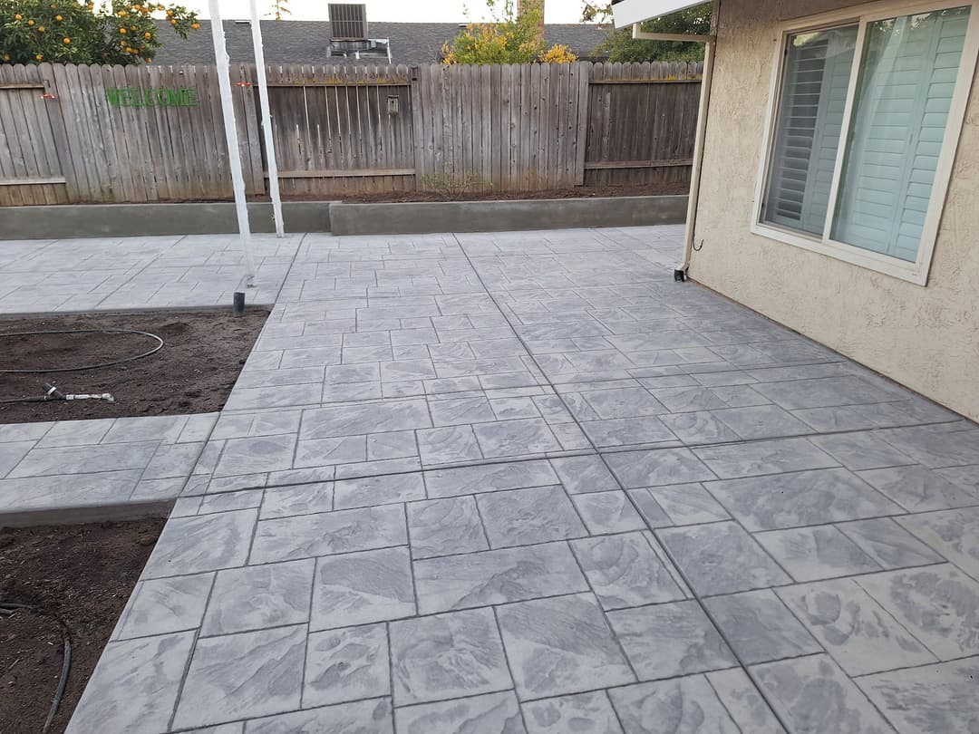 Decorative stamped concrete patio with landscaped background and fence.