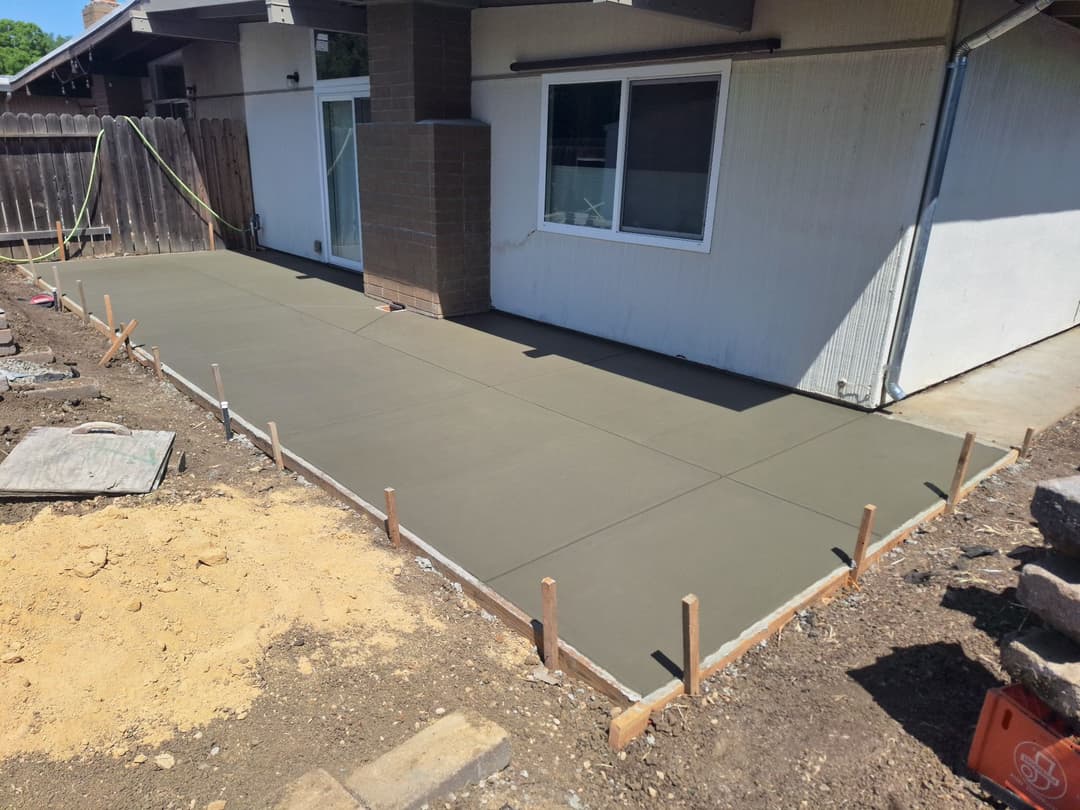 Concrete patio installation in a backyard, freshly poured and leveled, ready for finishing.